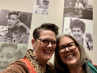 Bonnie Jean Feldkamp and Amy Sherman pose together in front of photos of Erma Bombeck in the Archives at the University of Dayton. Photo Credit: Bonnie Jean Feldkamp 