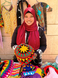  A Nubian woman displaced from her homeland by the building of the Aswan High Dam and the flooding of Lake Nasser displays her handmade artwork and crafts. Photo courtesy of Phil Allen. 