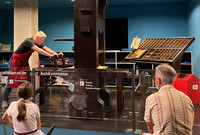 . A docent in Mainz, Germany, demonstrates to international visitors how the original Gutenberg printing press would have worked. Photo courtesy of Lesley Sauls Frederikson. 