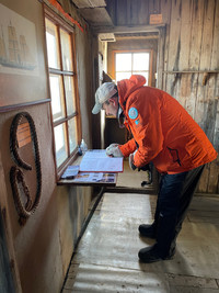  A visitor signs the guest log in tiny Nordenskjold's Hut on Snow Island in Antarctica where six researchers in the Heroic Age of Antarctica Exploration were stuck for 22 months. Photo courtesy of Lesley Frederikson. 